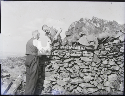 2 men stacking stones on large wall	