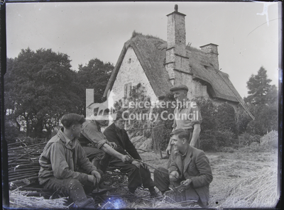 5 young men sitting outside house splitting branches on log