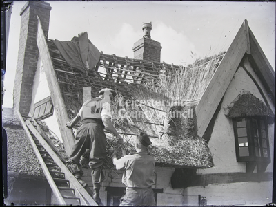 Thatcher handing another man on ladder thatch-stakes 		