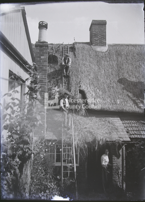 2 thatchers sitting on ladder; chimney to left	