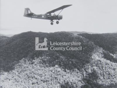 Auster aircraft in flight over forested hill