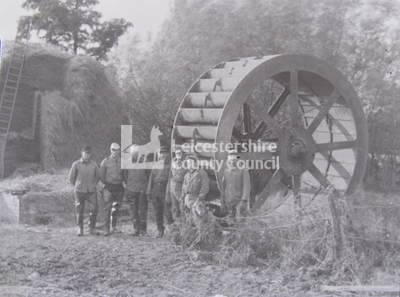 7 men standing with large waterwheel	