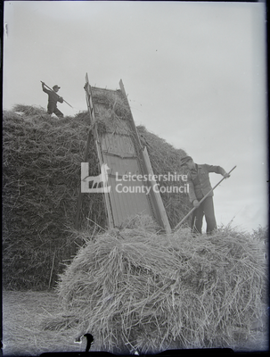 2 men (POWs) loading hay onto cart with elevator