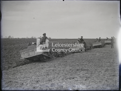 Men and boys riding ploughs across field
