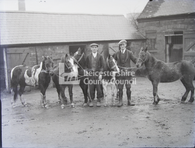2 men in stable yard holding 5 ponies