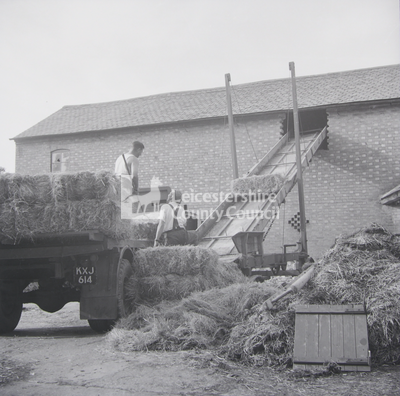 Two men loading hay-bales into barn with elevator