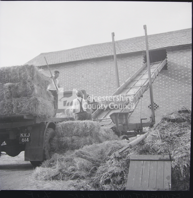 Two men raising hay bales to barn with elevator