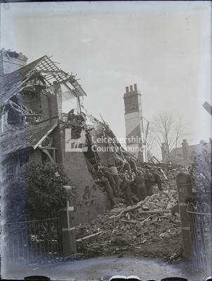 Group of uniformed men climbing rubble by bombed house